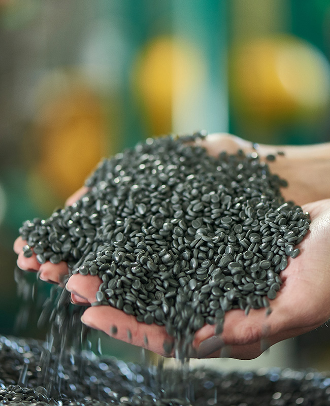 Deux mains tenant des granulés de plastique gris